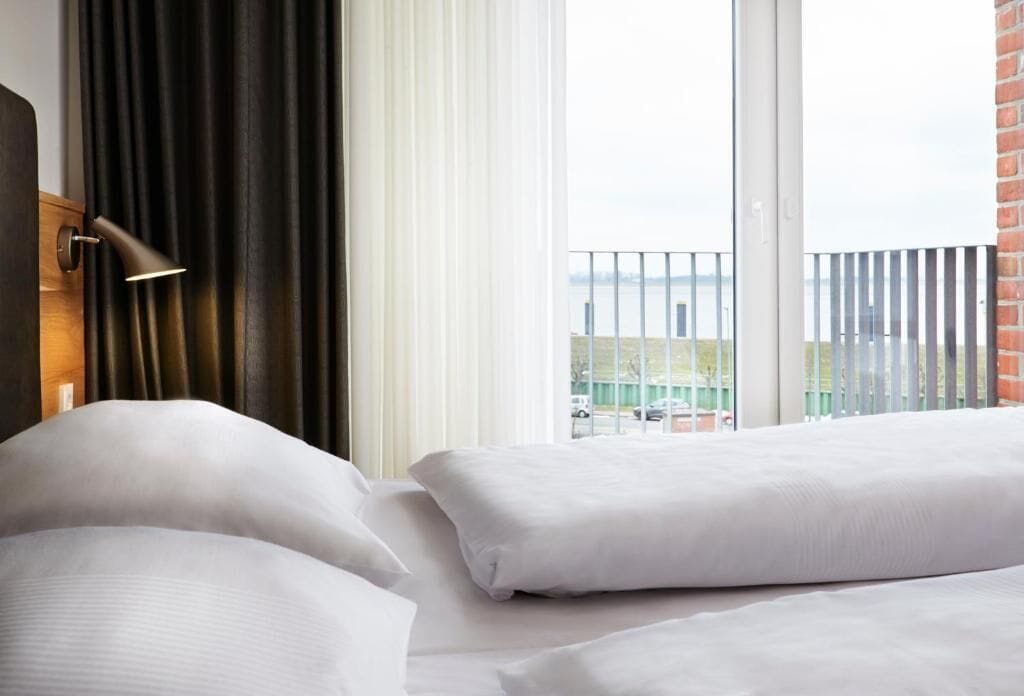 Habitación de hotel con cama, ventana con cortinas y vista a un edificio de la calle.