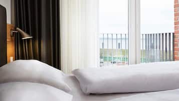 Habitación de hotel con cama, ventana con cortinas y vista a un edificio de la calle.