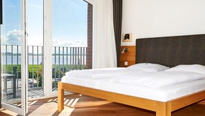 Une chambre avec un lit en bois, une vue sur l’extérieur grâce à une porte-fenêtre coulissante, et une petite table de chevet avec une lampe.