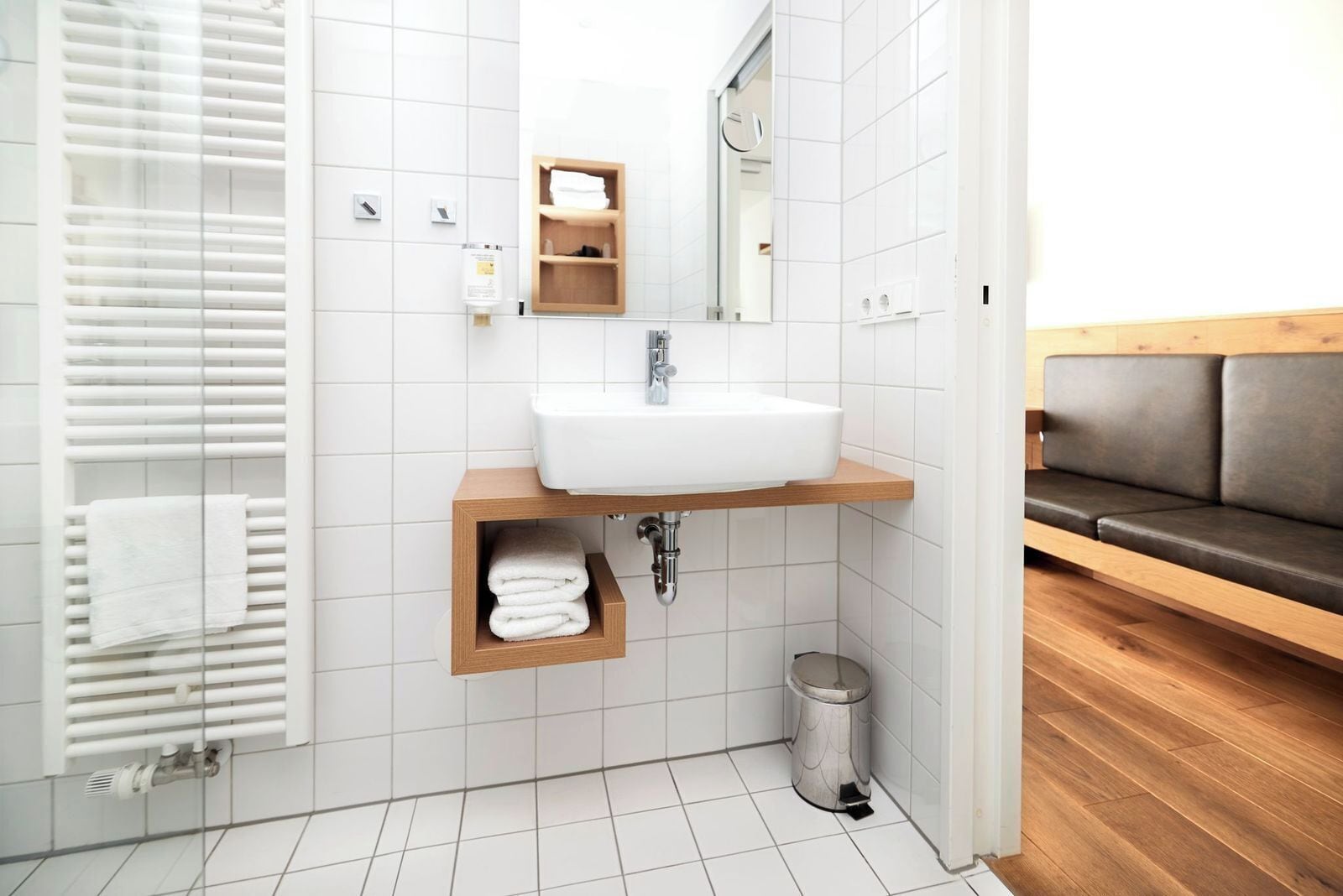 A modern bathroom with a white sink, wooden vanity, a mirror, and a towel rack.