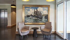 Un hall d’entrée avec deux fauteuils en cuir, une petite table ronde et un grand tableau encadré représentant un navire, accroché au mur.