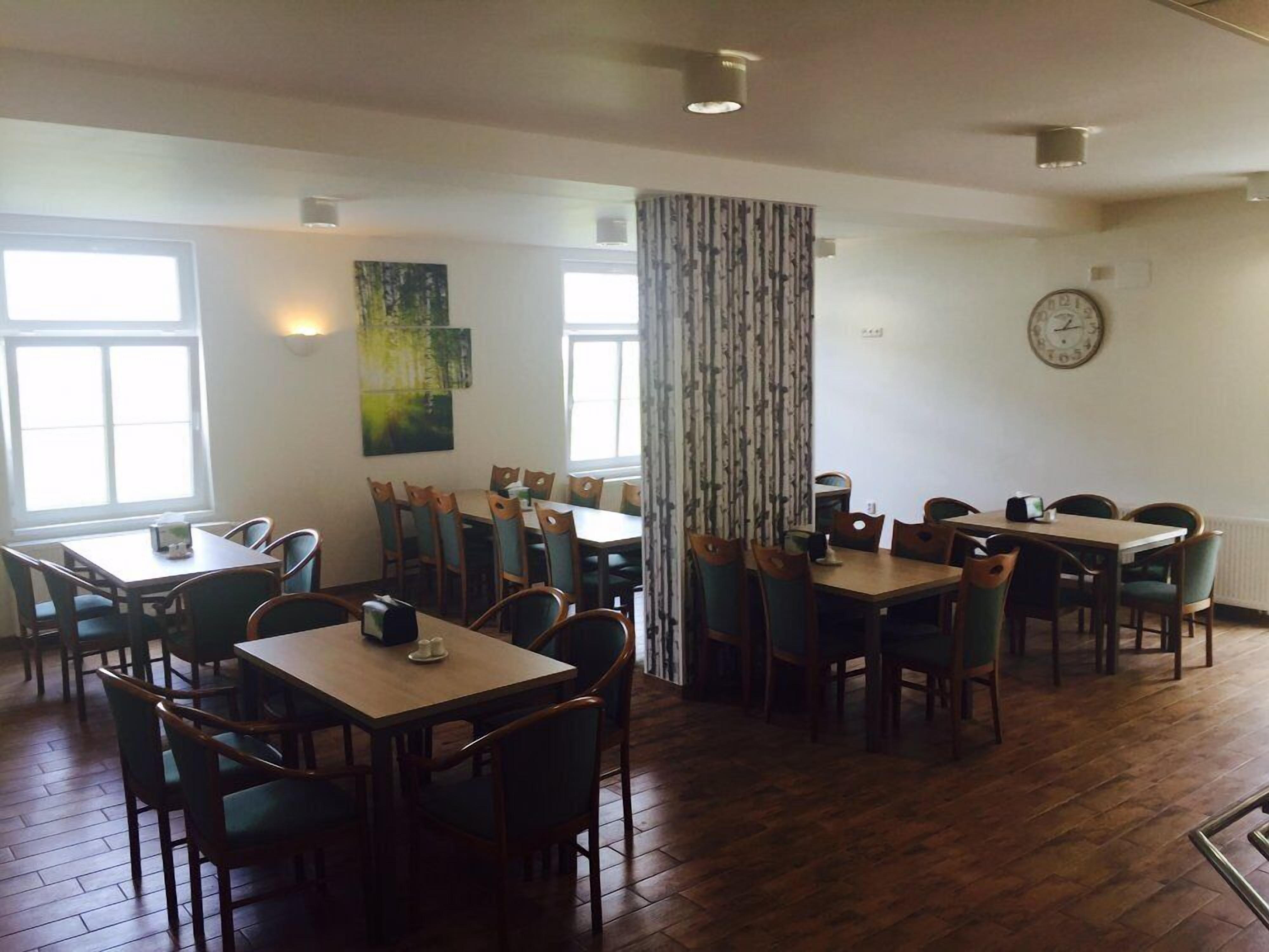 A dining area with multiple tables and chairs, large windows, and a clock on the wall.