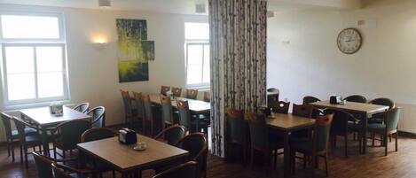 A dining area with multiple tables and chairs, large windows, and a clock on the wall.