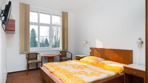 A bedroom with a bed, a desk, a chair, a window, and a radiator.