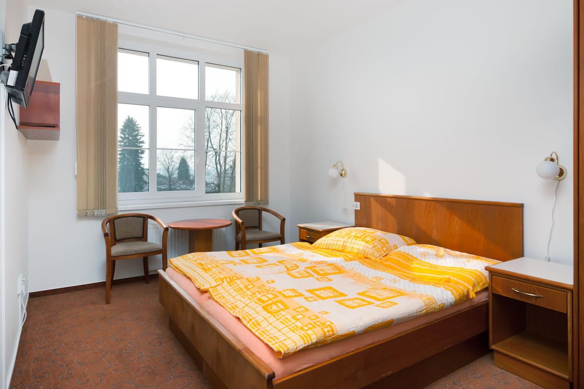 A bedroom with a bed, a desk, a chair, a window, and a radiator.