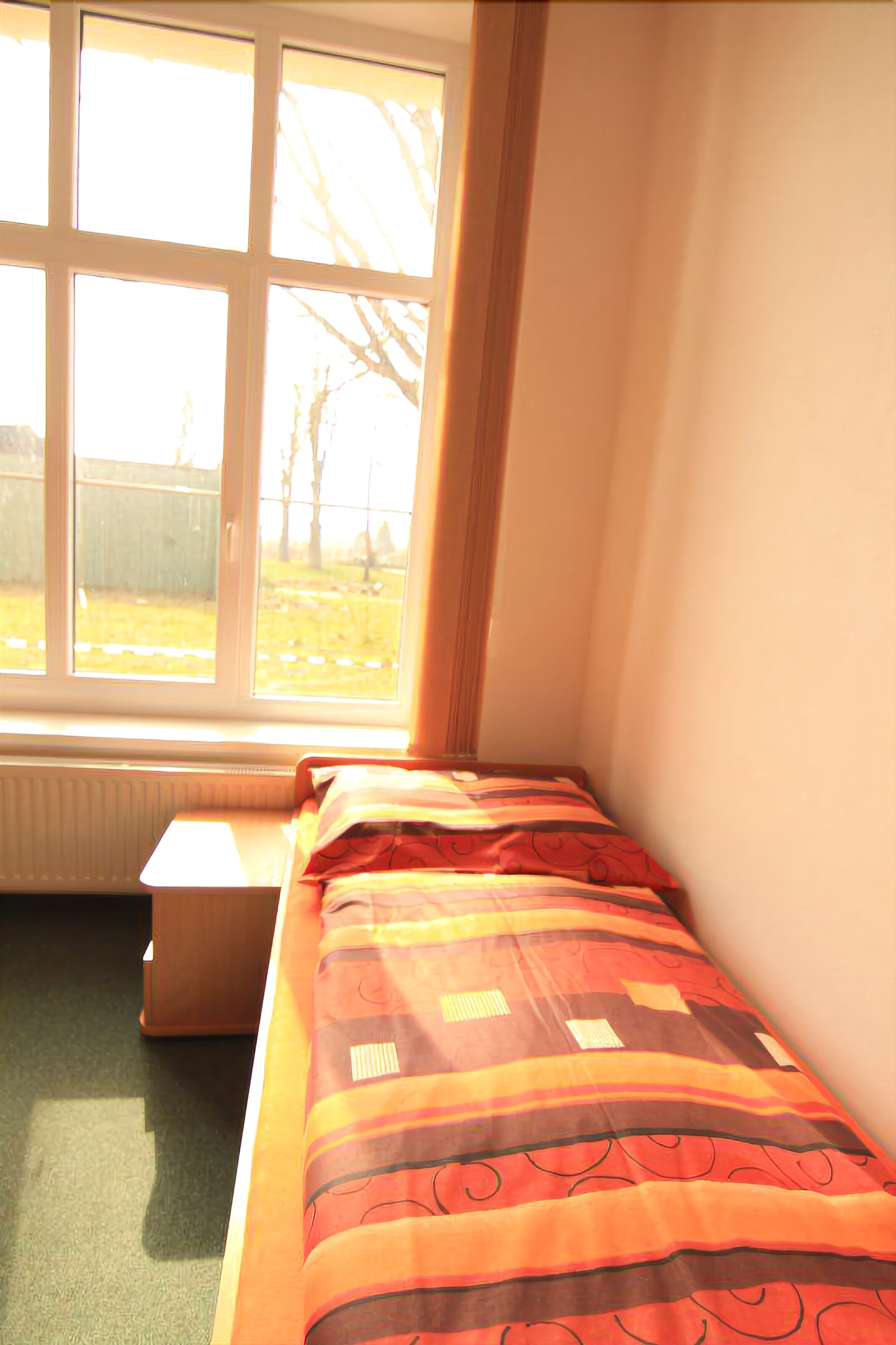 A small room with a single bed, a radiator, and a window with a view of a yard.