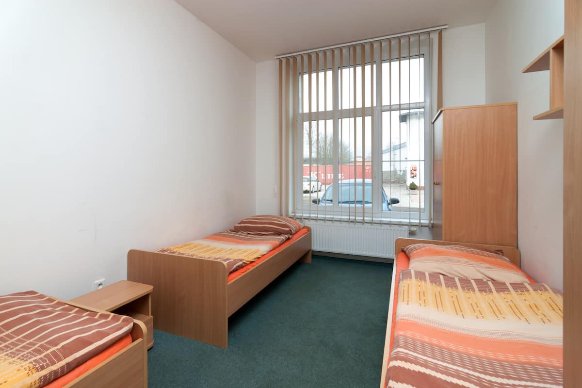 A room with two single beds, a wooden wardrobe, a window with blinds, and a radiator.