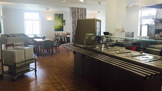 A spacious dining area with wooden flooring, a buffet station with multiple serving lines, and a seating area with tables and chairs.