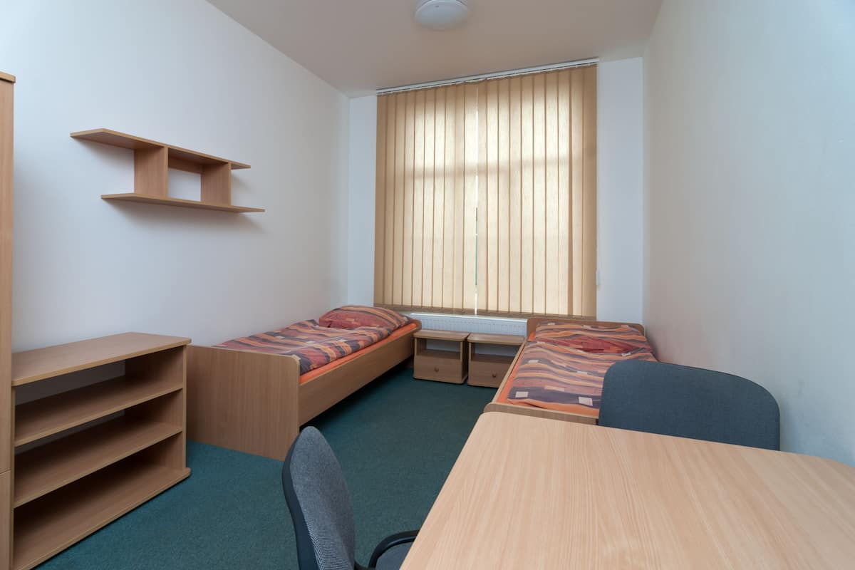 A compact room with two single beds, a desk, and a chair.