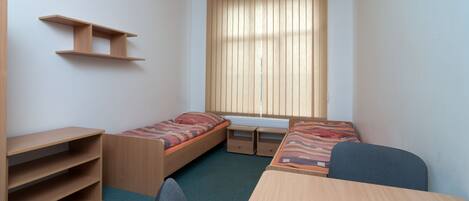 A compact room with two single beds, a desk, and a chair.