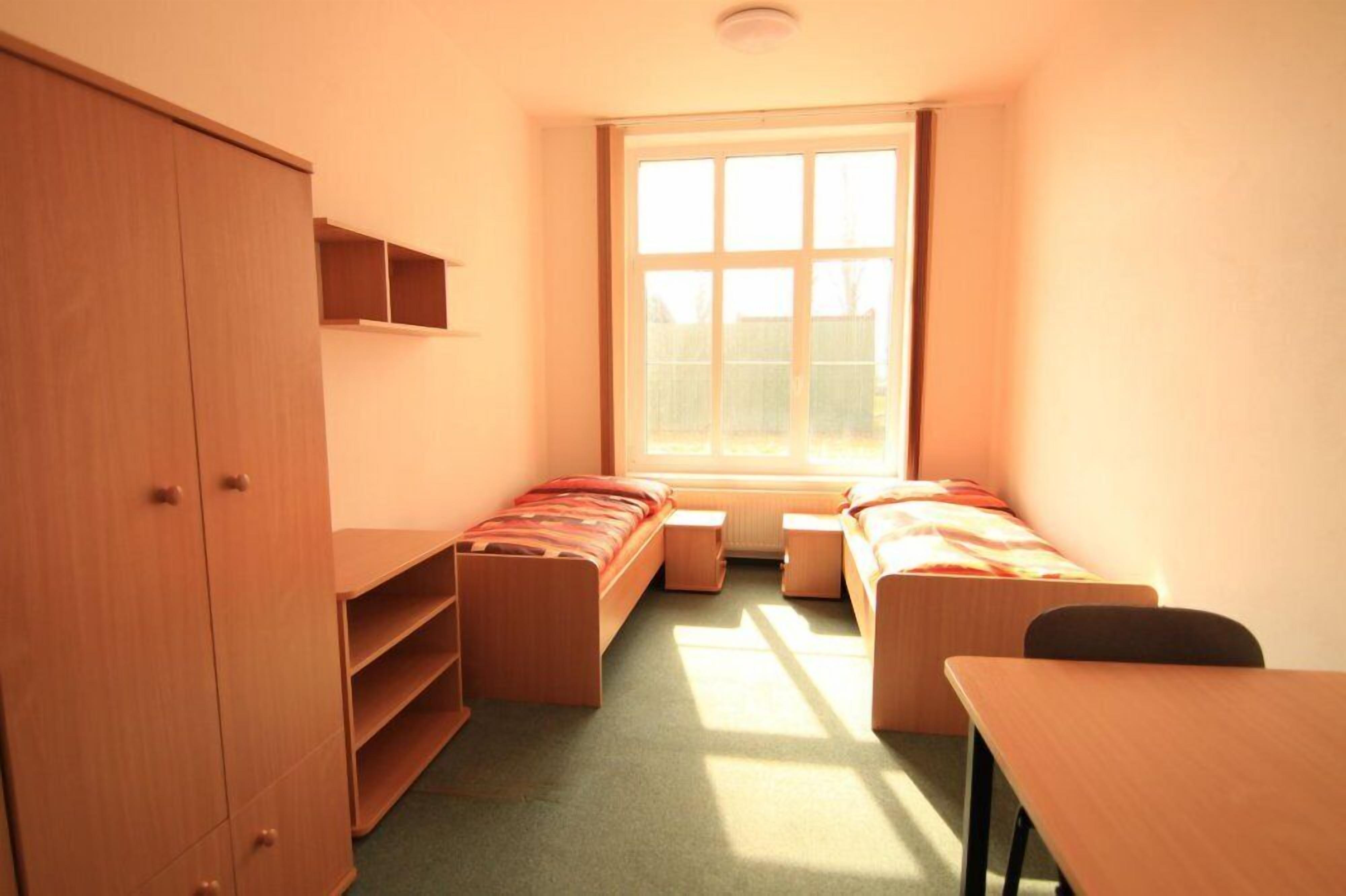 Een studentenkamer met een stapelbed, een bureau, een stoel, een kledingkast en een raam.