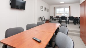 A conference room with a long wooden table, several chairs, a television mounted on the wall, and framed pictures on the wall.