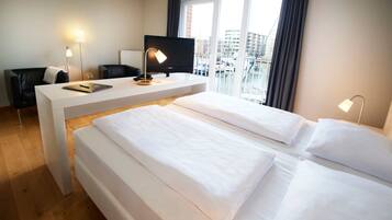 Ett hotellrum med två sängar, ett skrivbord, en stol, en TV och utsikt över staden genom stora fönster.