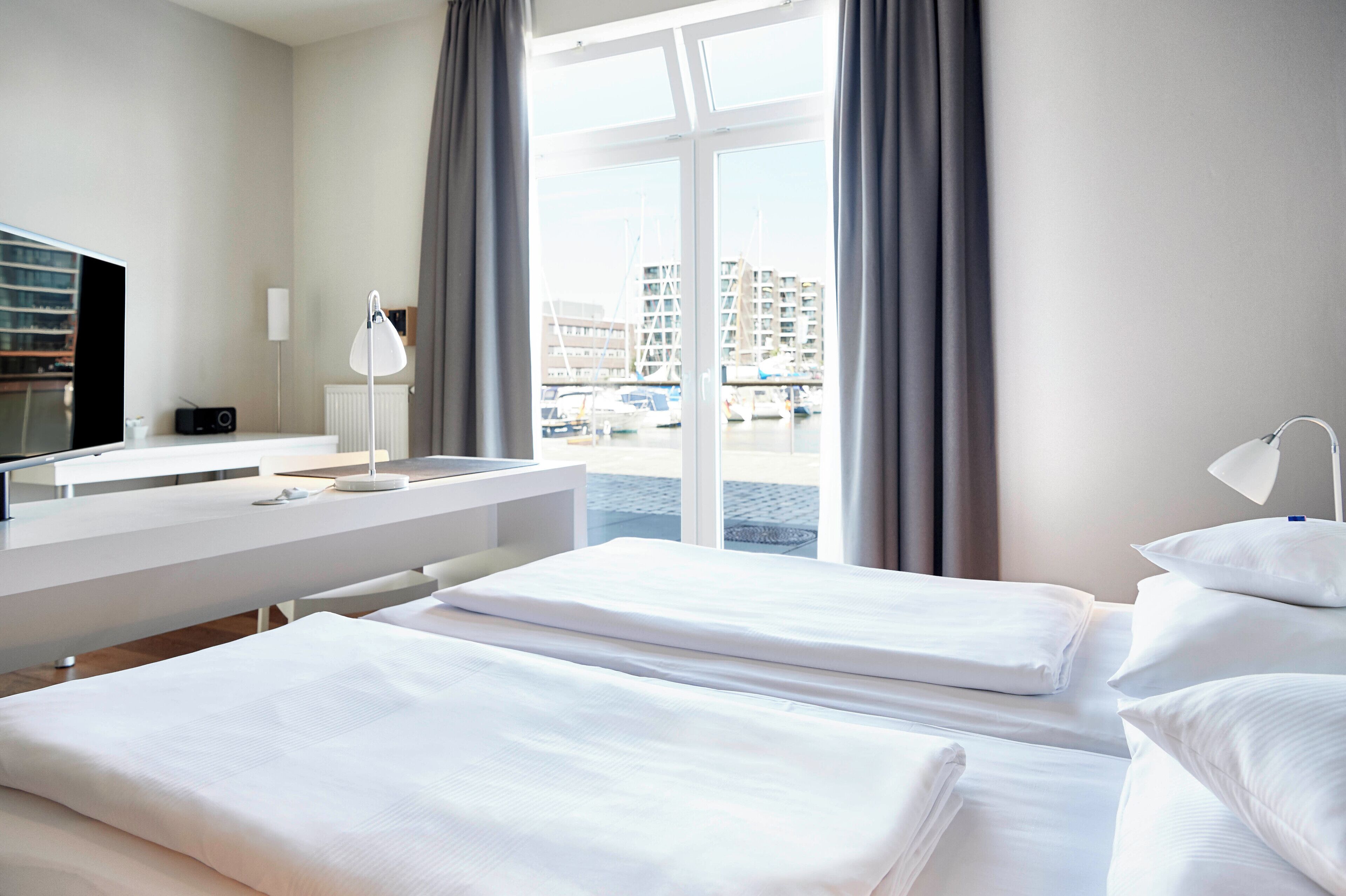 Habitación de hotel con dos camas, un escritorio, un televisor y vistas a un puerto deportivo.