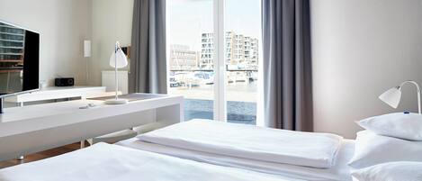A hotel room with two beds, a desk, a TV, and a view of a marina.