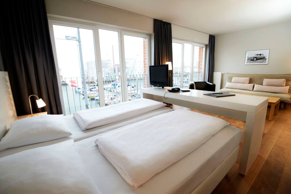 Ein Hotelzimmer mit zwei Betten, einem Schreibtisch mit Computer, einem Fernseher und einem Sofa.