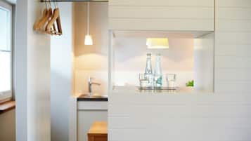 A kitchen with a hanging wooden rack, a sink, and a countertop with glassware and bottles.