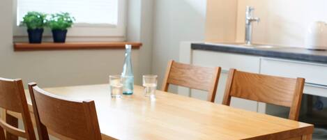A wooden dining table with four chairs, a bottle, and two glasses on it.
