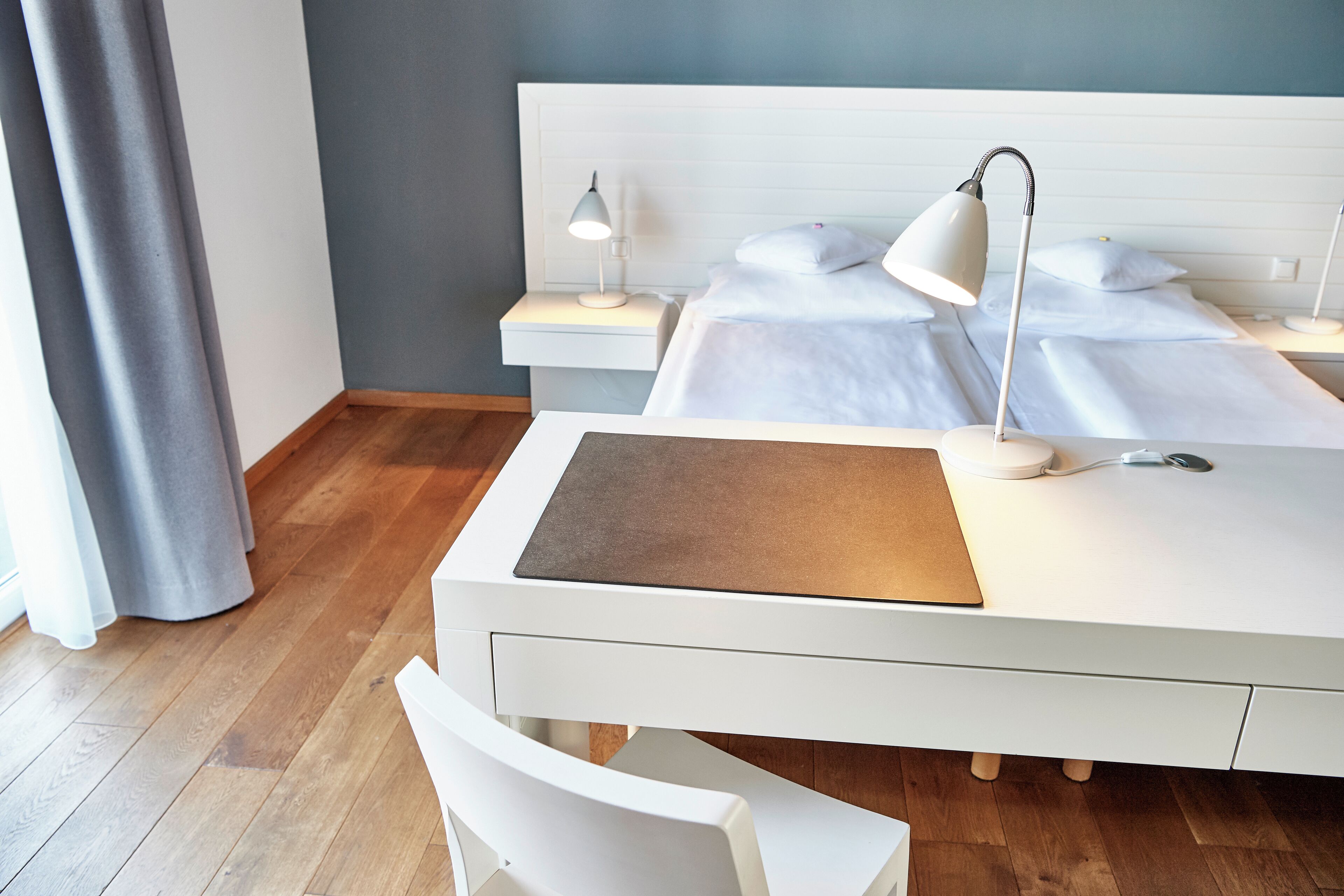 A neatly arranged bedroom with a bed, bedside tables, a desk, and a chair.