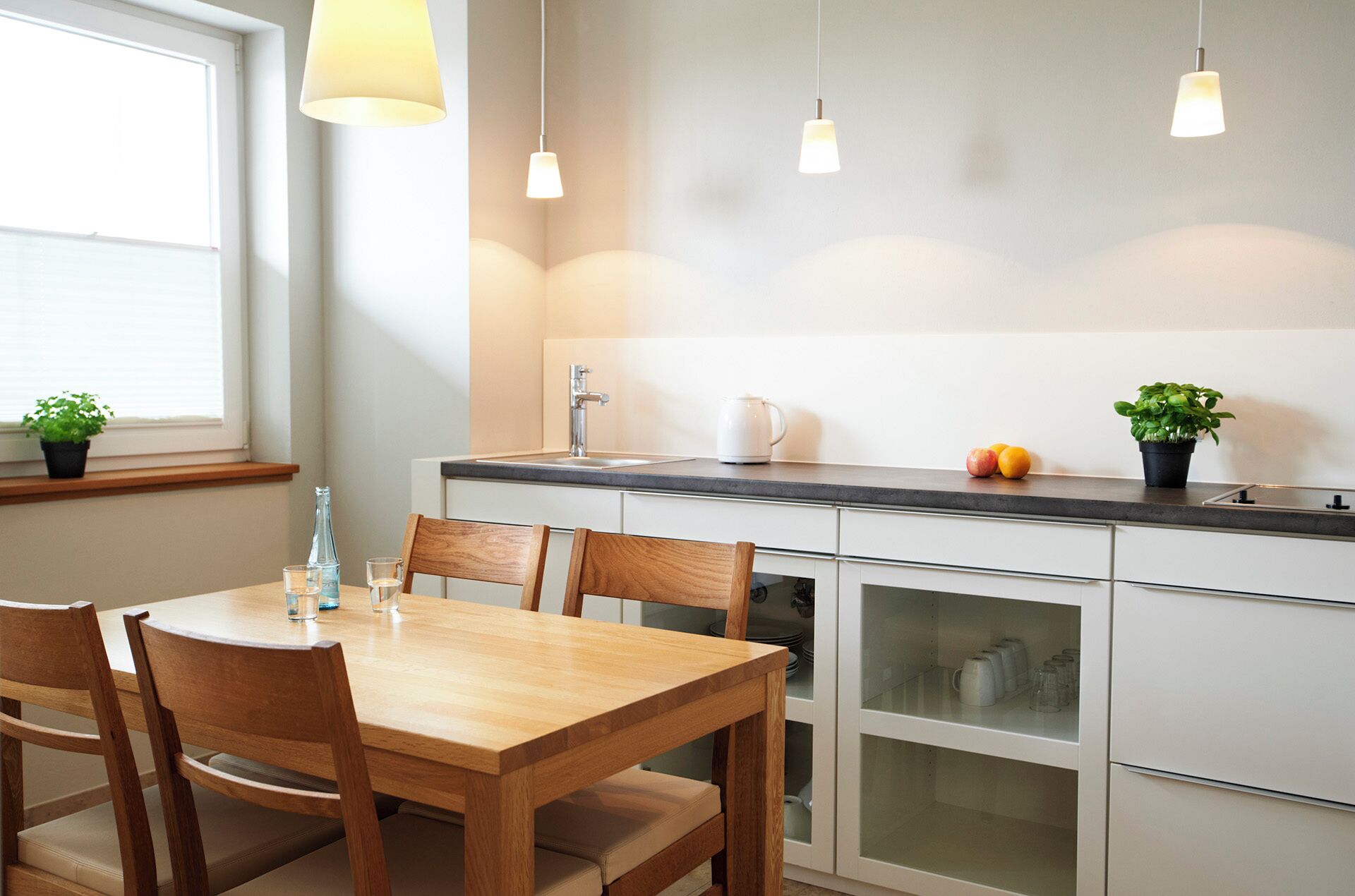Una cocina moderna con una mesa de comedor de madera, armarios blancos y luces colgantes.