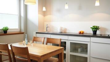 Een moderne keuken met een houten eettafel, witte kastjes en hanglampen.