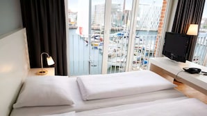 Hotellihuone, jossa on kaksi sänkyä, televisio, työpöytä ja näköala venesatamaan.