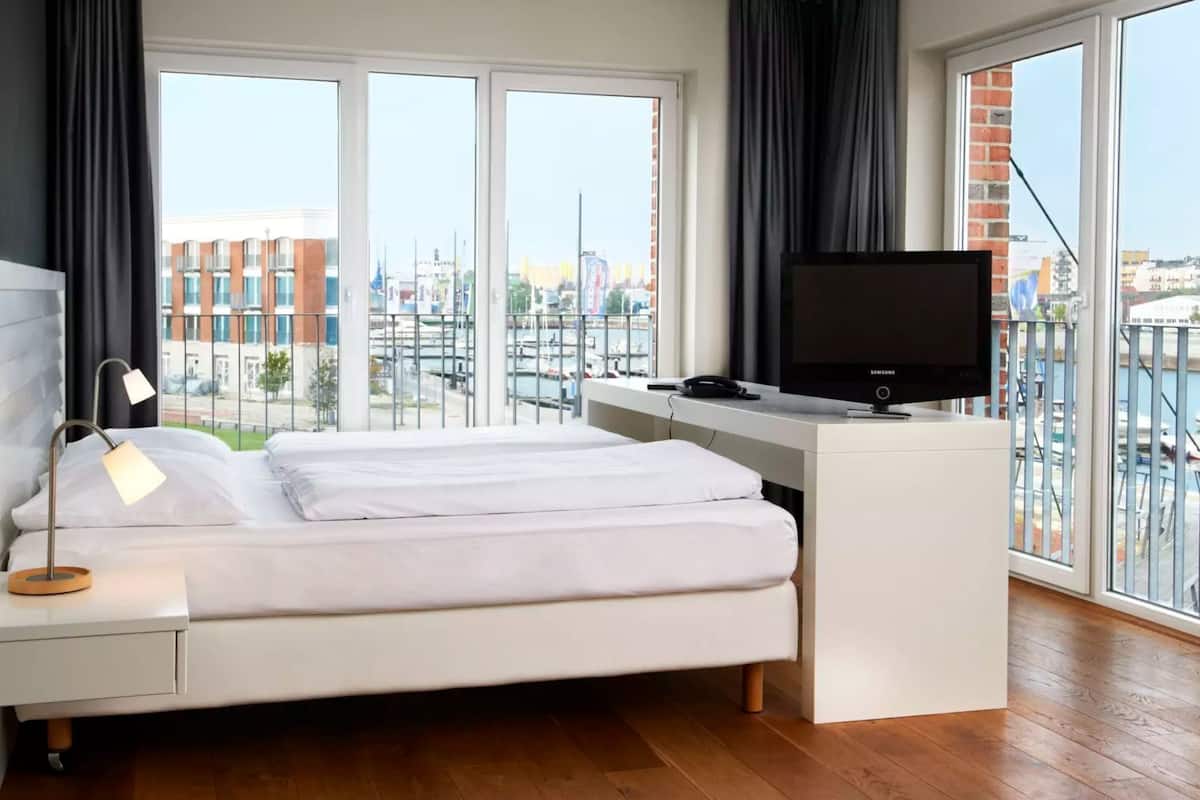 Ein modernes Schlafzimmer mit Bett, Schreibtisch, Fernseher und großen Fenstern mit Blick auf die Stadt.