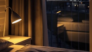 Hotellihuone, jossa on sänky, yöpöytä, lamppu ja näkymä toiselle rakennukselle veden yli.