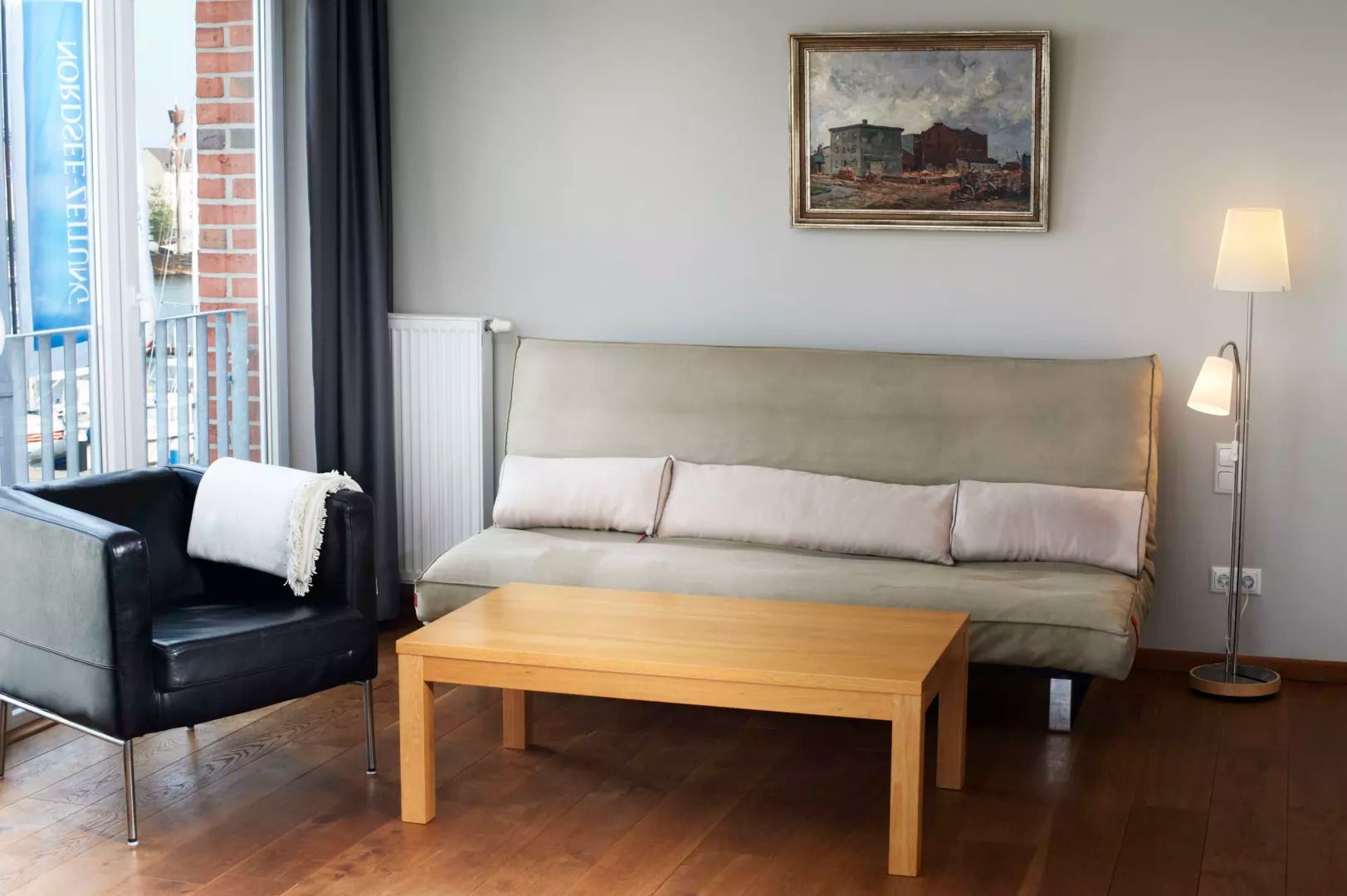 A living room with a sofa, a black armchair, a wooden coffee table, a floor lamp, and a painting on the wall.