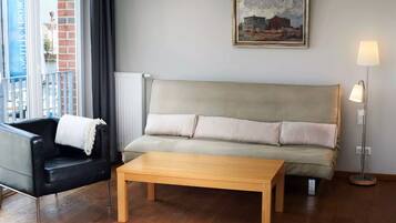 A living room with a sofa, a black armchair, a wooden coffee table, a floor lamp, and a painting on the wall.