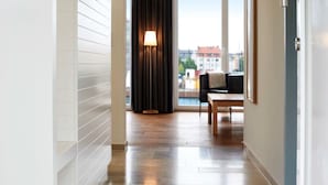 Moderni hotellikäytävä, jossa on puulattia, suuri ikkuna, josta on näkymä rakennuksiin, ja ikkunan lähellä oleva lamppu.