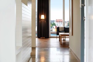 Ein moderner Hotelkorridor mit Holzboden, einem großen Fenster und Blick auf Gebäude sowie einer Lampe nahe am Fenster.