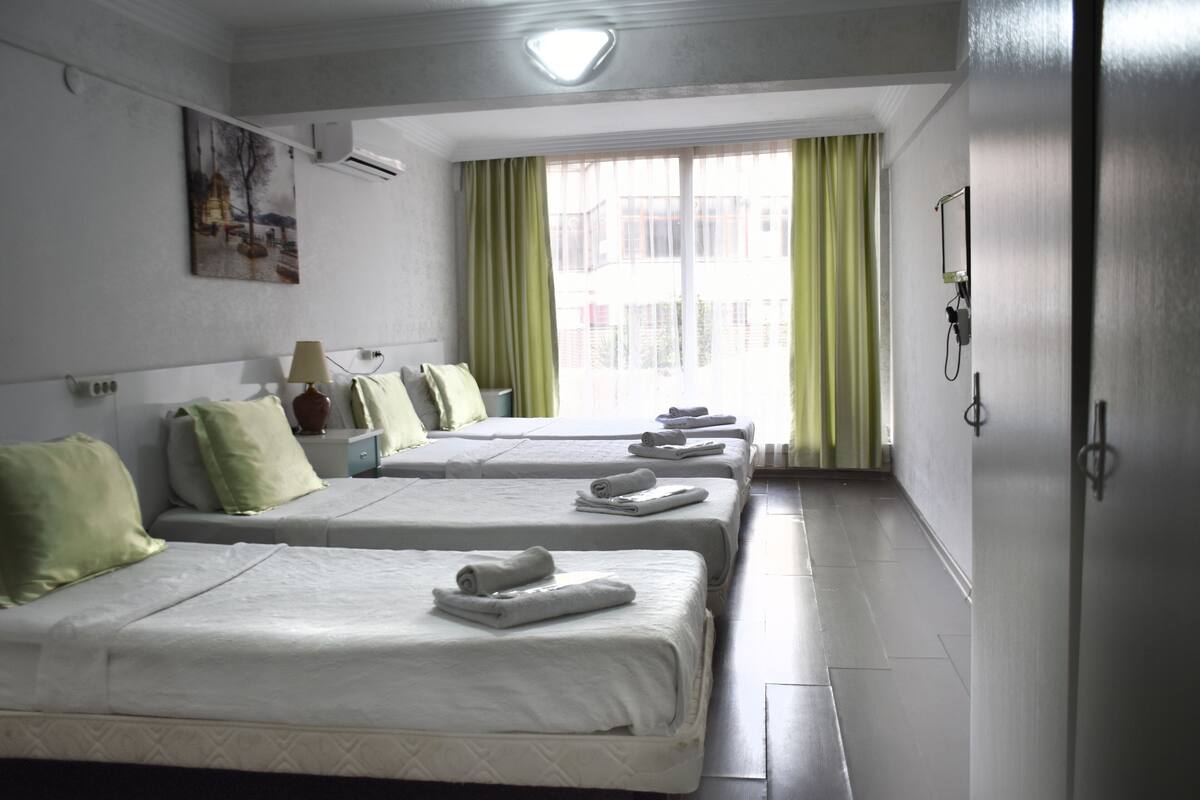 A hotel room with two beds, a bedside table with a lamp, a painting on the wall, and a window with curtains.