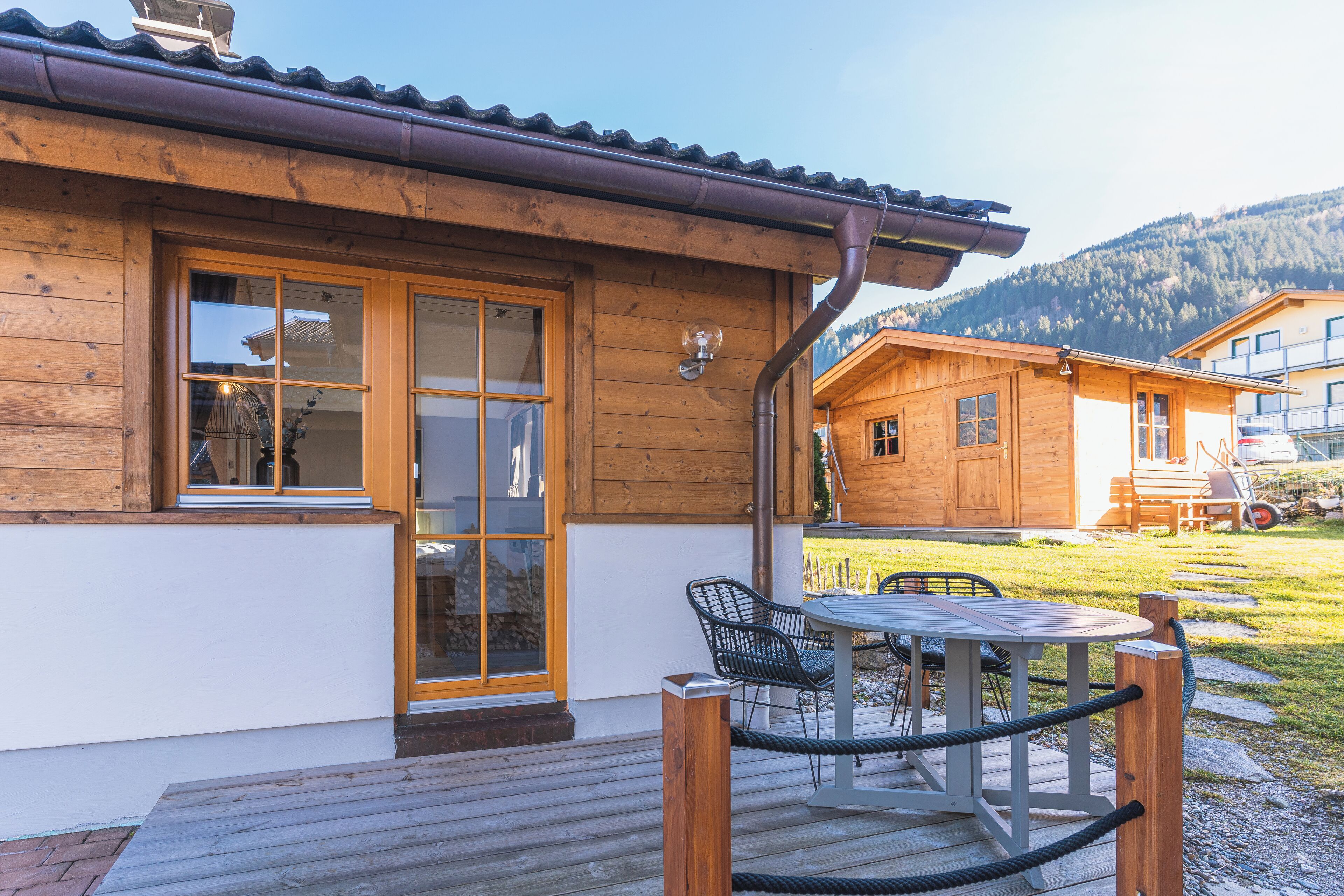 Een houten hut met een terras, een tafel met stoelen en een berg op de achtergrond.