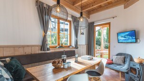 A cozy cabin interior with a wooden dining table, a bench, a sofa, and a fireplace. - Dorfchalets Kaprun (Kaprun)