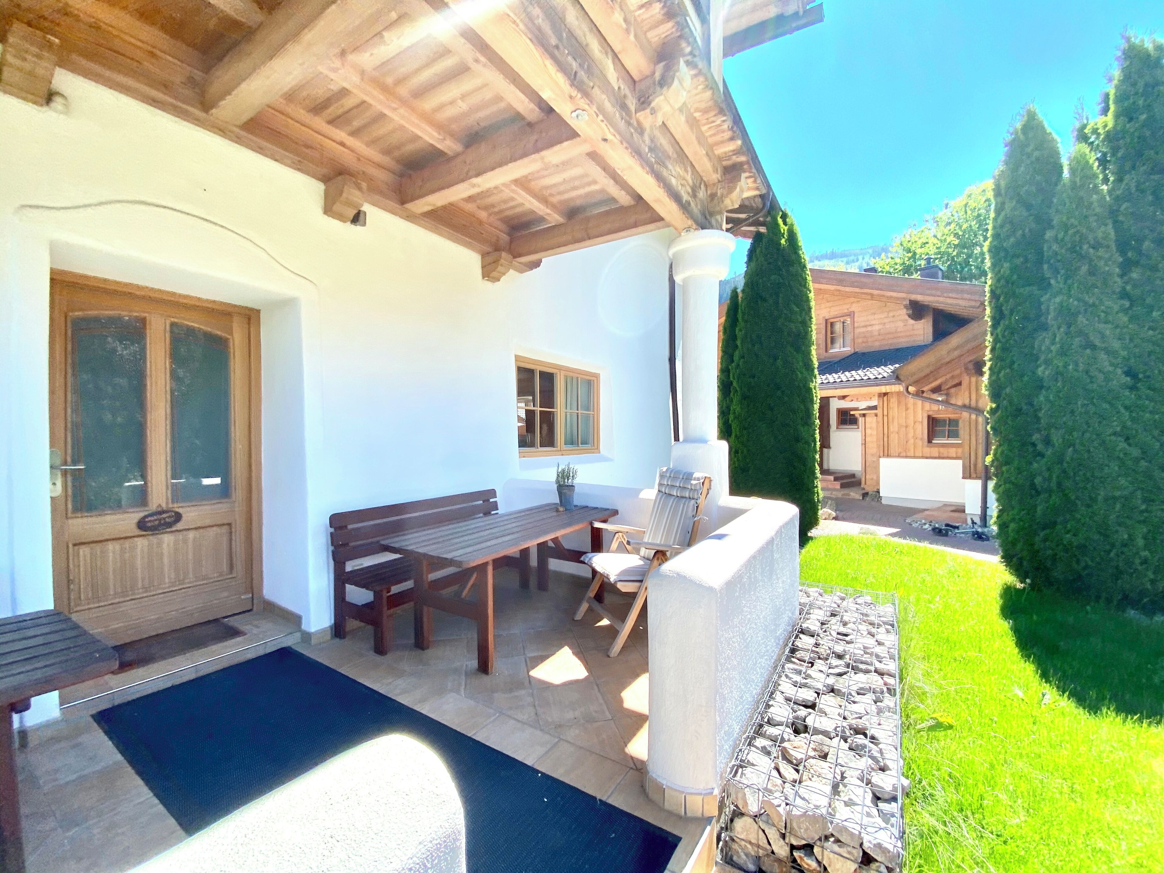 Une terrasse avec une table et des chaises en bois, un banc, une porte et une fenêtre.