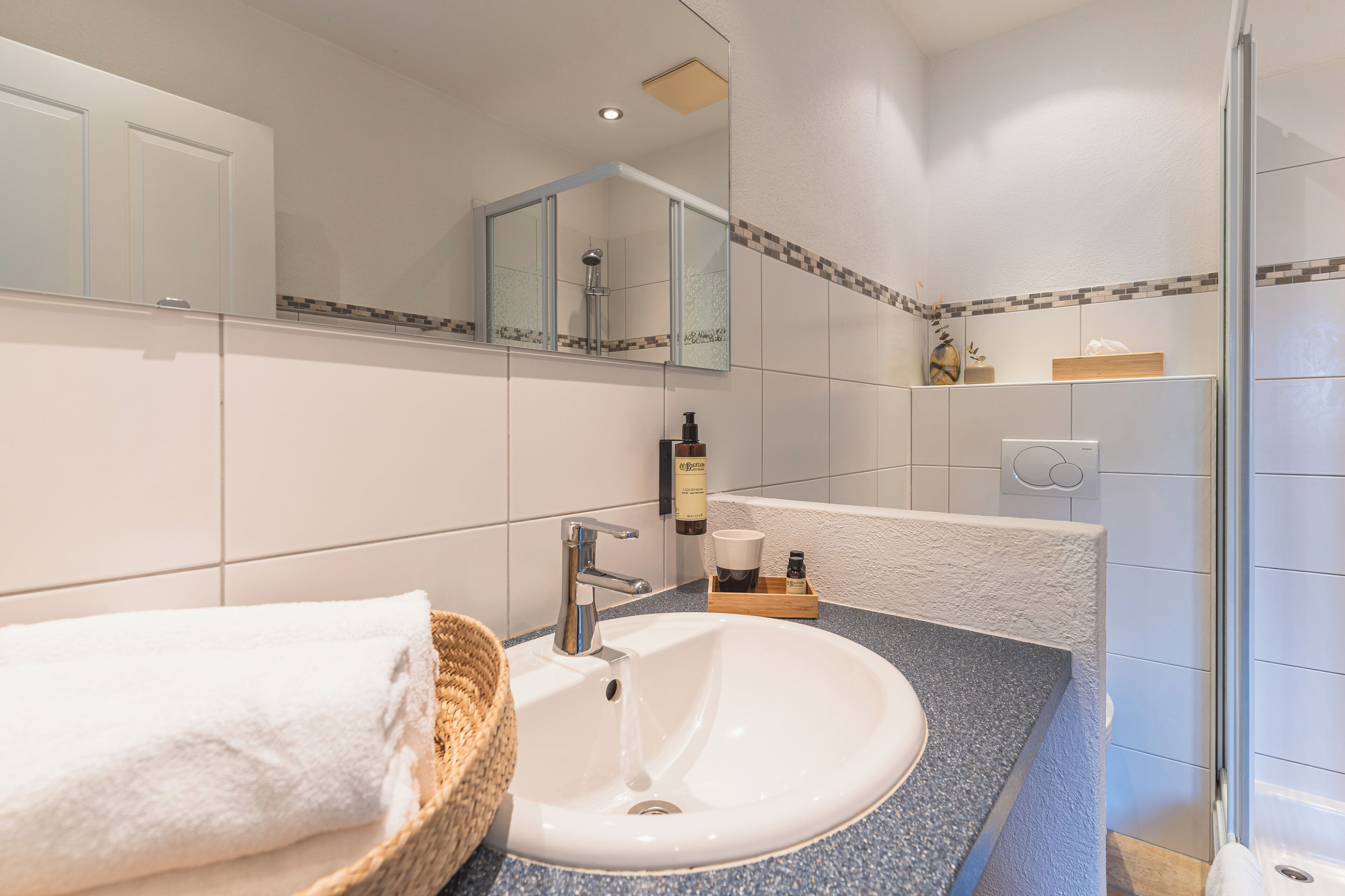 A bathroom with a white sink, a mirror, a shower, and a towel on the counter.