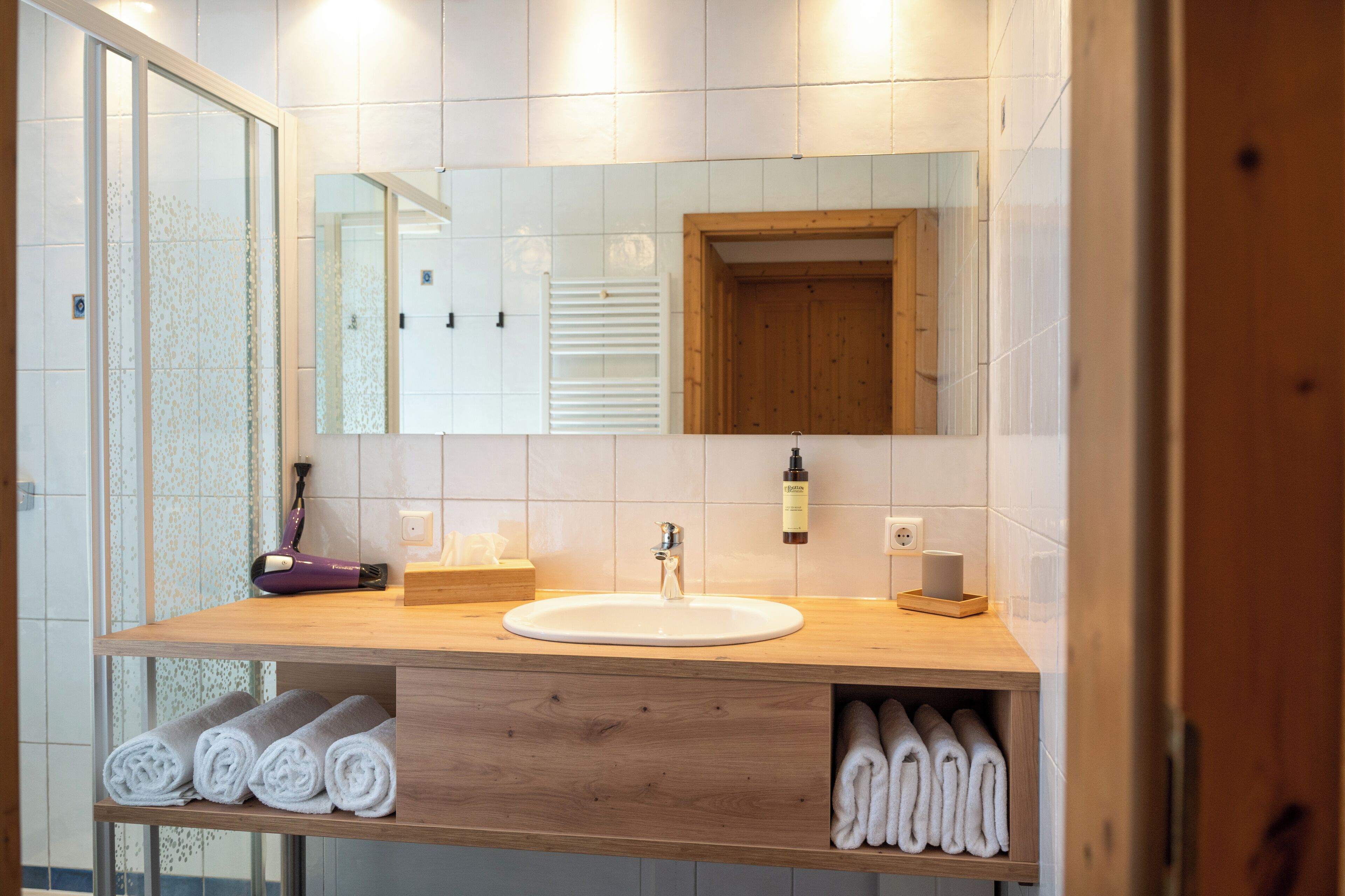 Een moderne badkamer met een houten wastafelmeubel, een grote spiegel en netjes opgerolde handdoeken.