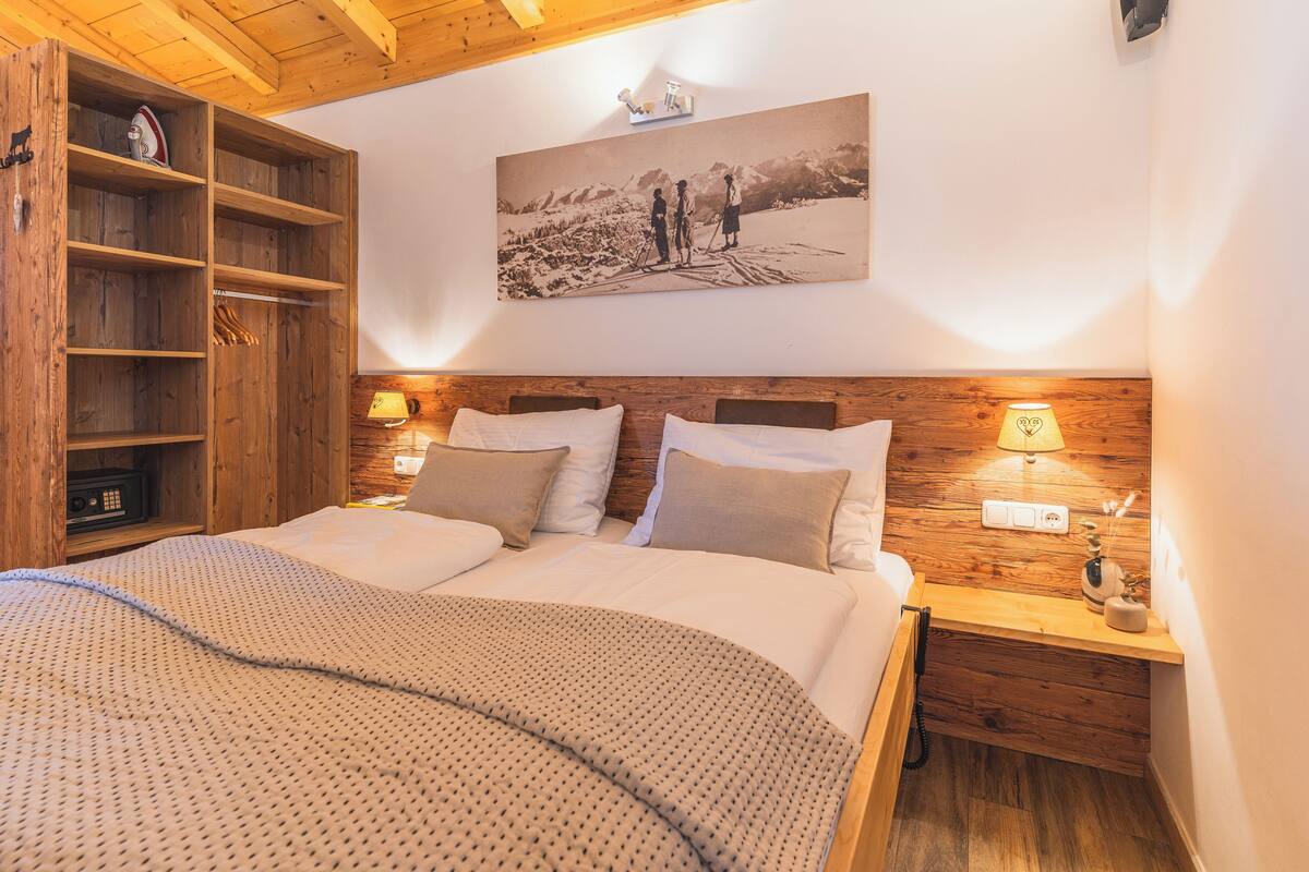 A bedroom with a wooden headboard, a bed with white linens, a wooden nightstand with a lamp, and a shelf with a picture frame.
