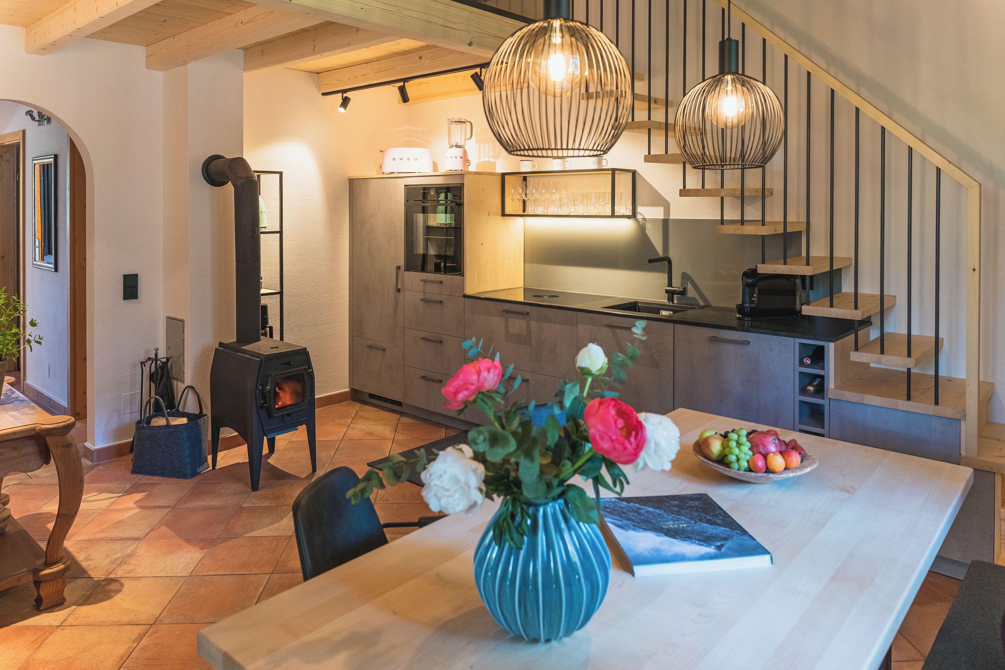A modern kitchen with a central island, a dining area with a vase of flowers, and a staircase leading to an upper level.