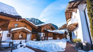 A snow-covered village with wooden buildings, a brick pathway, and mountains in the background. - Dorfchalets Kaprun (Kaprun)