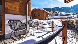 A wooden building with a snow-covered porch and two metal chairs. - Dorfchalets Kaprun (Kaprun)