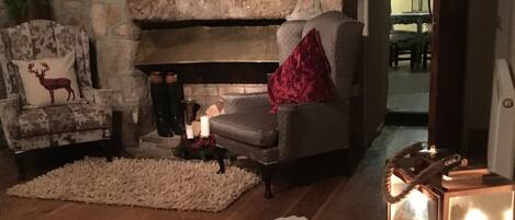 A cozy living room with a stone fireplace, a plush armchair, and a coffee table with magazines.