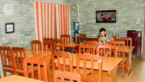 A dining area with multiple wooden tables and chairs, a water dispenser, and a television mounted on the wall. - Hotel Delight Inn (Pokhara)