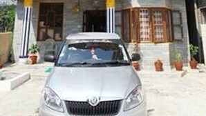 A silver car parked in front of a building with a yellow and white facade, a stone exterior, and a window with a wooden frame. - Hotel Delight Inn (Pokhara)