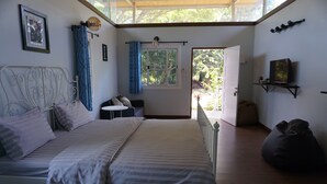 A bedroom with a bed, a small table, a chair, a bean bag, a window with curtains, and a door leading outside. - Sonseesaed Farm (Phu Ruea)