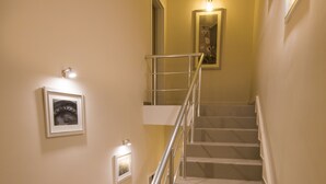 Una escalera con barandilla de metal, paredes color crema y dos lámparas fijadas a la pared.