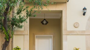 Entrada de un edificio con una puerta blanca, un colgador de luz negro y dos macetas a cada lado de las escaleras.
