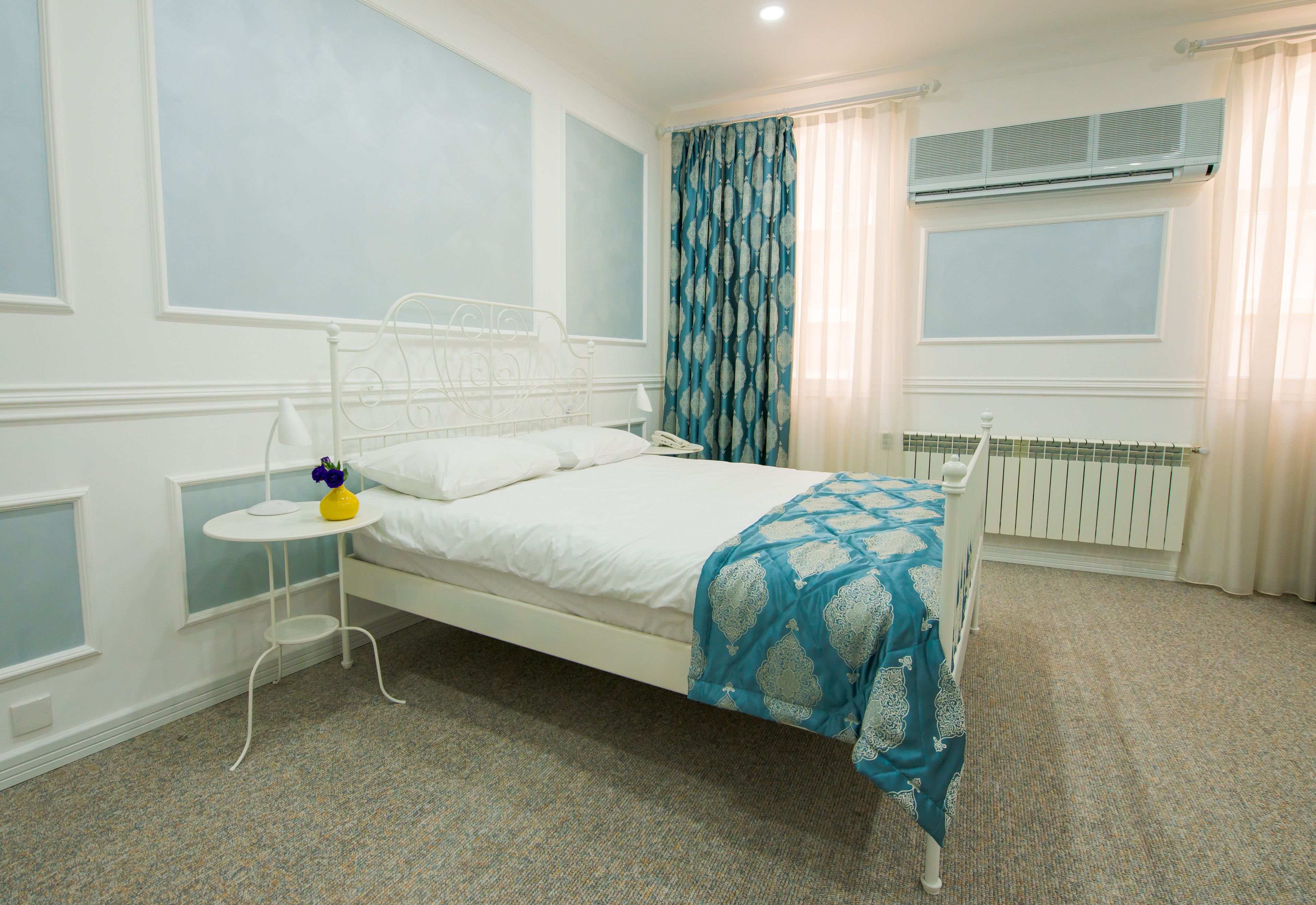 Ein ordentlich eingerichtetes Schlafzimmer mit einem Einzelbett, einem Nachttisch mit Lampe und einem Fenster mit Vorhängen.