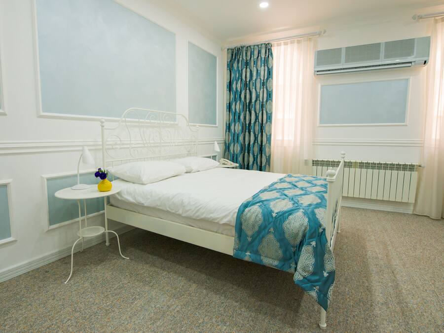 Ein ordentlich eingerichtetes Schlafzimmer mit einem Einzelbett, einem Nachttisch mit Lampe und einem Fenster mit Vorhängen.